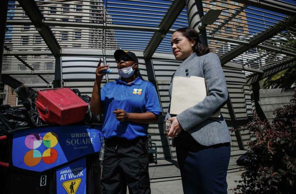 A Block by Block employee in a blue uniform at Union Square speaks to a business woman.