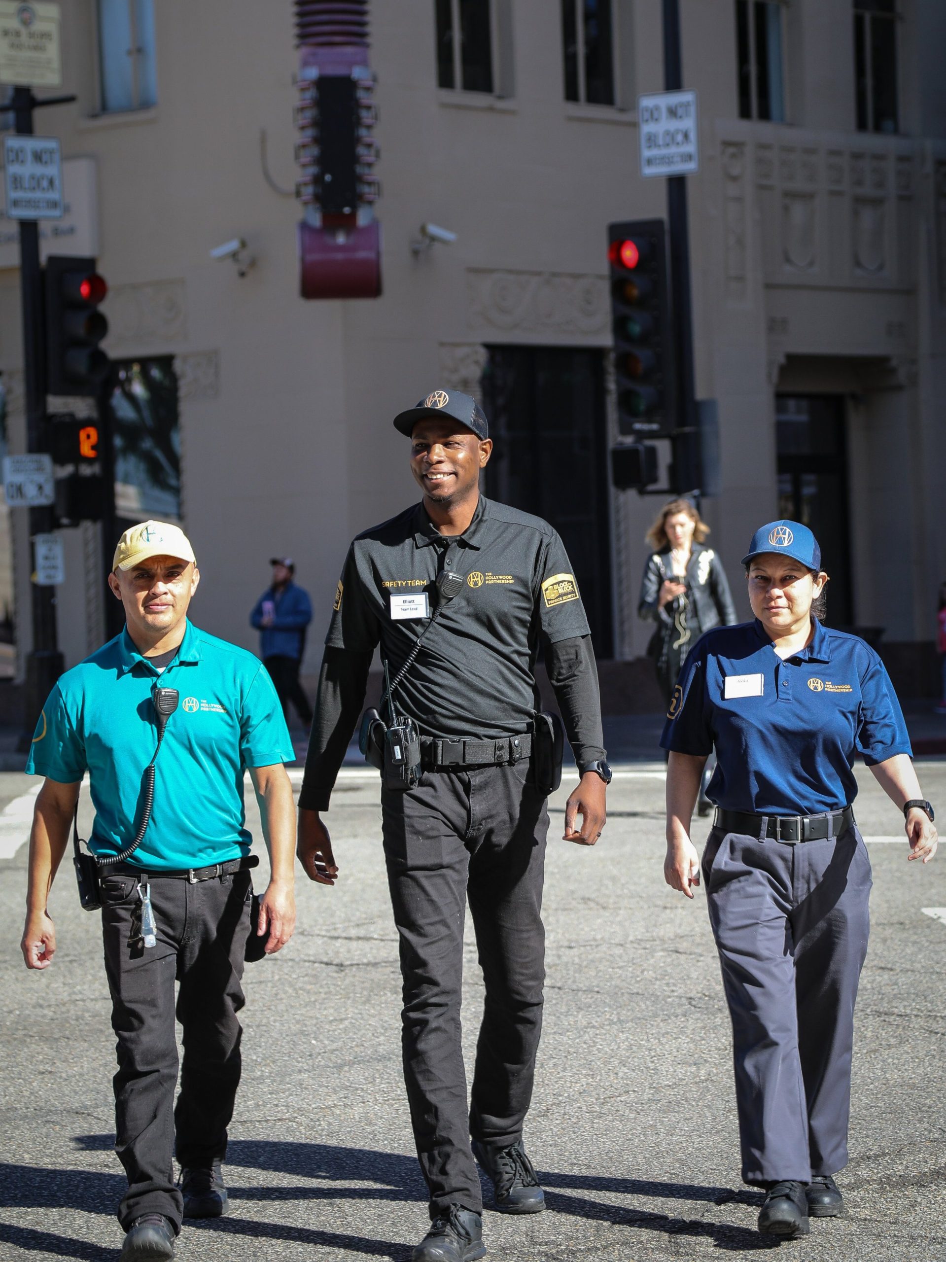 Three Hollywood Partnership Ambassadors dressed in different uniforms walk down the street, smiling.